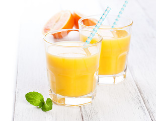 Summer yellow orange lemonade in glass with blood oranges and straw on a wooden table, closeup.