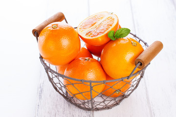 Fresh juicy summer blood oranges in a vintage basket with mint leaf on wooden table on a white...