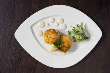 Beautiful fresh golden fish cakes, served with a wedge of lime, dill sauce and rocket on a white plate