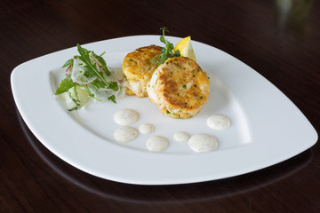 Beautiful fresh golden fish cakes, served with a wedge of lime, dill sauce and rocket on a white plate