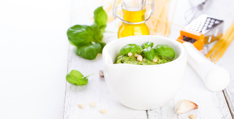 Homemade traditional basil pesto with olive oil, cedar nuts and garlic in a white bowl on a wooden rustic table on a white background with copy space or place for text, closeup