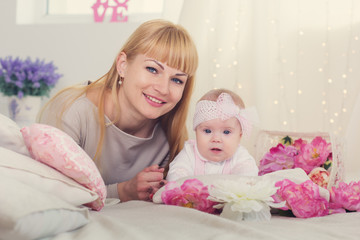 Mother and daughter are lying on bed with pink flowers