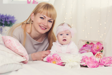 Mother and daughter are lying on bed with pink flowers