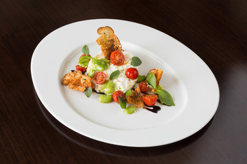 Delicious tomato and mozzarella cheese salad caprese, served on a white plate, with basil, croutons and balsamic vinegar.