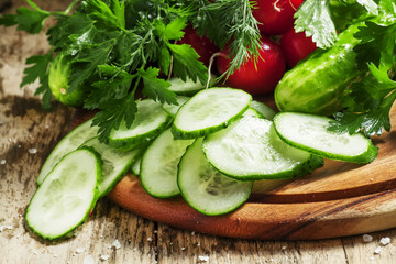 Sliced cucumber, vegetables and herbs, old wooden background, se