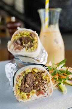 Mexican shredded beef breakfast burrito sliced in half served with ice coffee.