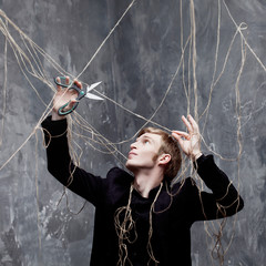Young man tries to cut the straps with scissors. The concept of liberation from manipulation