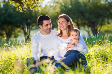 Fototapeta premium Parents holding their little son, sitting on the grass
