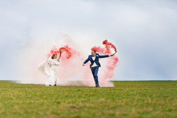 Жених и невеста бегут по полю с красными дымовыми шашками на фоне облаков © meatbull