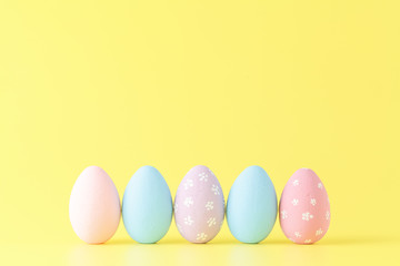 Easter eggs painted in pastel colors on yellow paper background