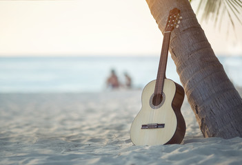 An acoustic guitar standing in the sandy beach under palm tree
