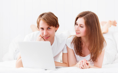 happy couple with laptop on internet in bed