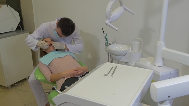 Young Doctor is Examining a Teeth of a Patient Dentist in Mask is Sitting Behind a Client Woman and Working Concentratedly at Dental Treatment Room