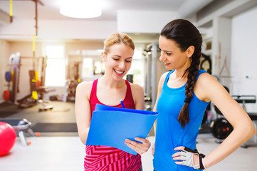 Woman in gym, personal trainer, consultiing plan on clipboard