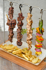 Cooked Chicken, beef and vegetable kebab skewers hanging from a rack, served with fries, and ready to eat.