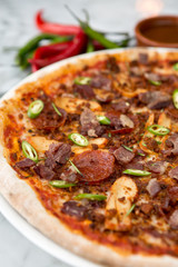 Spicy pepperoni, chicken and bacon pizza with jalape–o slices and chilli peppers in the background