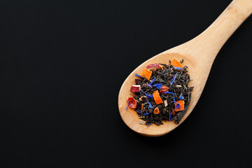 assortment of dry tea in wooden spoon, on black background