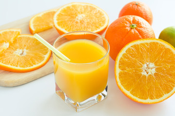 Fresh orange juice in the glass with tubule on the white background, near slices of orange