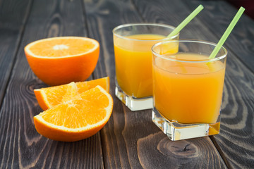 Fototapeta na wymiar Fresh orange juice in the glasses with tubule with orange havel on a brown wooben table. Selective focus