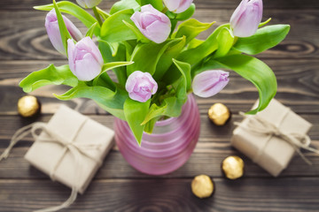 bouquet of purple tulip in the pink vase with gift boxes and can