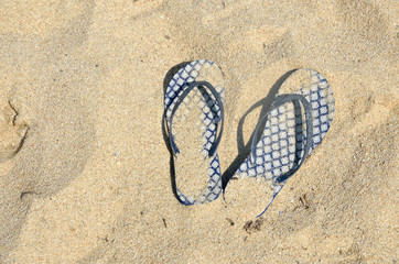 Fototapeta na wymiar Blue flip flops covered with sand left on beach