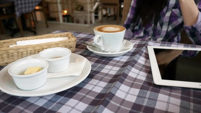 Close up of table in the restaurant. There is tablet pc, coffee, bread and butter.