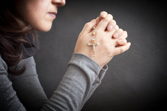 Woman Praying With Rosary Over Dark Background