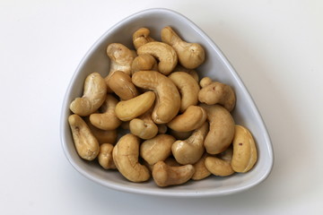 Raw cashew nuts in a white bowl, isolated on white background