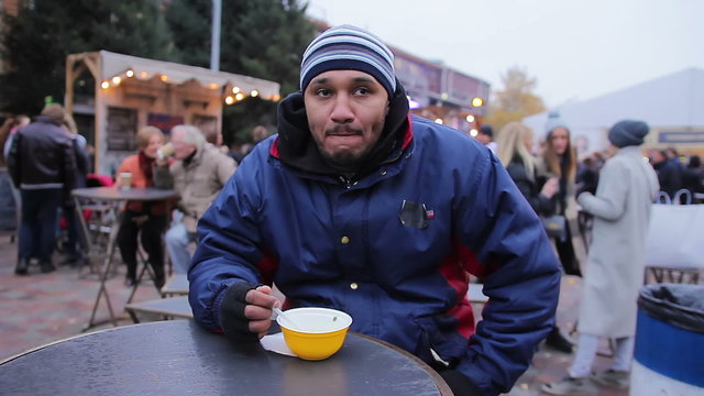 Hungry man eating tasty soup at street food festival. Loneliness and sadness