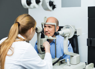 Female optician doing eye examination with aid of slit lamp