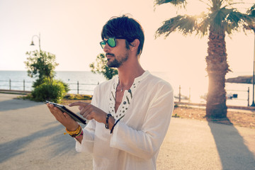Young hipster man with digital tablet by the sea