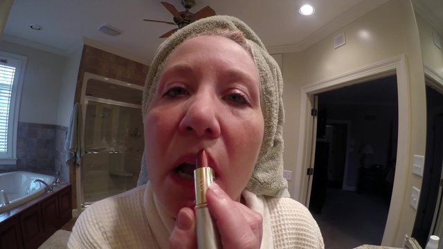 Mature woman wearing bathrobe in bathroom applying lipstick,