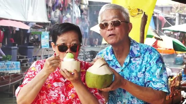 HD video of Asian senior couple travel to thailand floating market. Drinking fresh coconut juice