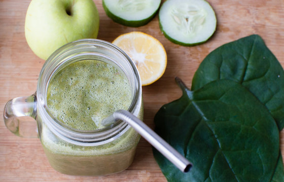 High angle view of green smoothie in glass mug with metal straw on bamboo tray with apple, lemon, cuumber and spinach (selective focus)