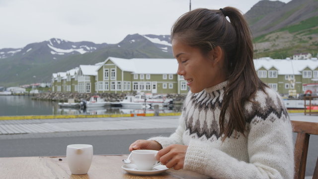 Tourist drinking coffee on sidewalk cafe on Iceland. Woman enjoying coffee from cup wearing icelandic sweater. People visiting iceland sitting outdoors in Siglufjordur, North Iceland. RED EPIC.