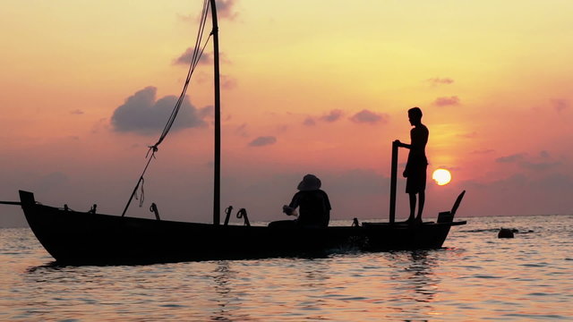 Two fishermen scooped water out of an old wooden boat at the end of a hard day at sunset in the Indian Ocean. Slow motion.