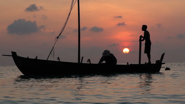 Two fishermen scooped water out of an old wooden boat at the end of a hard day at sunset in the Indian Ocean. Slow motion.