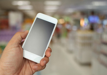 hand holding the smartphone on supermarket in blurry for backgro