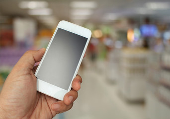 Fototapeta na wymiar hand holding the smartphone on supermarket in blurry for backgro