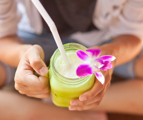 Cocktail smoothie decorated with orchid in the hands of women