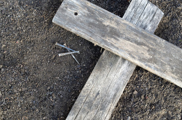 Wooden Cross laying on the earth with three nails laying nearby.