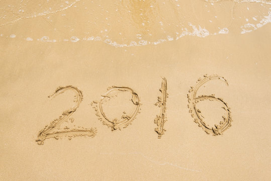 Year 2016 hand written on the white sand in front of the sea