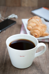dining table with hot coffee cup and croissant, office equipment on wooden floor.
