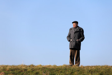 Elderly man standing on a wall in front of blue sky