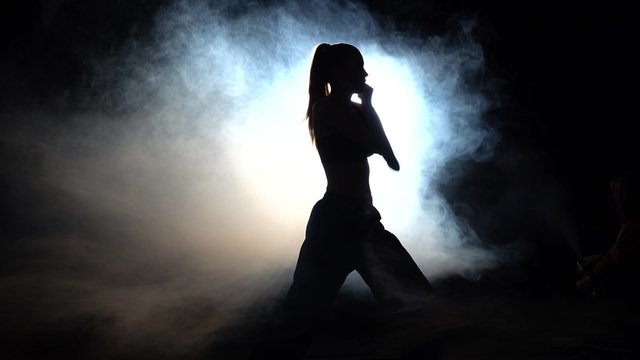 Girl athlete shows power moves. Black. Silhouette. Backlight