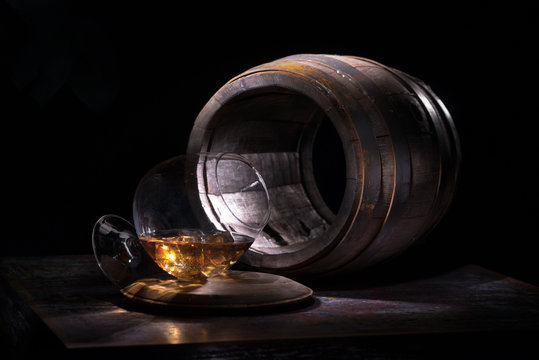 A glass of whiskey and ice against the backdrop of empty oak barrels