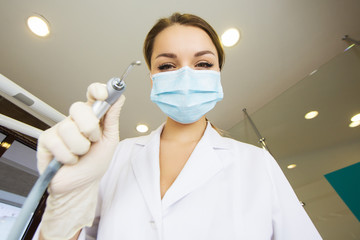 Fototapeta na wymiar young women dentist with sterile mask readily approaching a patient with dental instruments held in the hands protected with surgical gloves young dentist with sterile mask