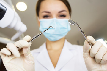 young women dentist with sterile mask readily approaching a patient with dental instruments held in...