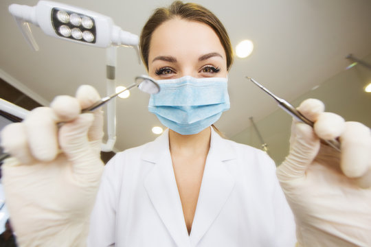 young women dentist with sterile mask readily approaching a patient with dental instruments held in the hands protected with surgical gloves young dentist with sterile mask