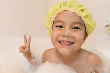 バブルバスの中で楽しむシャワーキャップをかぶった女の子、ピースをしてる。